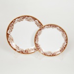) PORCELANA, dois (2) pratos de tamanhos distintos, ornados com barrado floral com predominância da tonalidade marrom, arremates com frisos a ouro, linha MON CHERI, marca RENNER (Porto Alegre, RS, fundada em 1942; em 1998 foi vendida para a Vista Alegre de Portugal; em 1999 mudou a razão social para Vista Alegre do Brasil), sendo: 1 para bolo, medindo 14,5 cm diâmetro e 1 para sobremesa, medindo 17,5 cm diâmetro, vide foto.