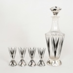 CRISTAL, conjunto com cinco (5) itens: 1 licoreira Art Deco, incolor e translúcida, facetado geometrizado, esmaltação na tonalidade preta, marca Moser (fundada em 1857 por Ludwig Moser na Bohemia, Karlovy Vary, atual República Tcheca), medindo 29,5 cm altura, acompanham 4 taças na mesma padronização, medindo 9 cm altura, todos os itens com fundo estrelado, vide foto.
