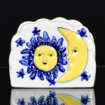 LOUÇA, um (1) porta guardanapo com ornamentação pintada a mão nas tonalidades azul e amarela, modelagem relevada representando sol, lua e estrelas, medindo 10,5 x 8 x 4,5 cm, sem marca de manufatura aparente, vide foto.