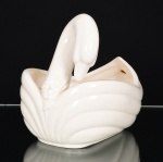 FAIANÇA, uma (1) floreira ou centro de mesa, modelada na forma de cisne, tonalidade branca, marca WEISS (São José dos Campos, SP, 1941 a 1995, empresa que nasceu da capacidade criativa de Inês Weiss, que desenvolveu uma pintura colorida e exuberante, inicialmente pintava peças da Fábrica Santo Eugênio, com a saída do seu marido Roberto Weiss e do seu cunhado Mário Weiss da Fábrica Santo Eugênio para fundar a Irmãos Weiss, Inês passou a decorar as peças artesanalmente entre os anos 40/60, da própria fabrica do marido e do cunhado, entre as décadas de 60/90 a produção foi industrializada), medindo 20 cm comprimento, apresenta o craquejado característico do envelhecimento de toda a faiança, vide foto.