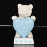 ESCULTURA, uma (1) animalista representando urso segurando um grande coração com a legenda: I Love You Grand Mother, confeccionada em biscuit, tonalidade azul e branca, sem marca de manufatura aparente, medindo 8,5 cm altura, vide foto.