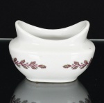 PORCELANA, uma (1) molheira com ornamentação policromada em elementos vegetalistas e laçarotes, marca SHENANGO CHINA  NEW CASTLE, PA, USA (constituída em 1901 na cidade de New Castle; em 1936 firmou acordo com Theodore Haviland Company de Limoges para produzir louças finas sob a marca American Haviland; em 1939 fez acordo semelhante com a Rosenthal alemã, sob a marca Castleton China Company; em 1954 virou Shenango China Incorporation; em 1960 virou Shenango Ceramics; em 1968 foi vendida para Pipe & Ceramics Corporation; em 1979 foi vendida para Anchor Hocking Corporation; em 1987 se fundiu com a Newell Company e virou subsidiária da Syracuse China; em 1991 encerrou as atividades), medindo 8,5 x 7,5 x 6 cm.