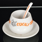 ) PORCELANA, uma (1) molheira com presentoir acoplado, acompanha a concha, feita para CUCA S, marca Porcelana SÃO PAULO (fundada no ano de 1940 em São Caetano do Sul, SP, pelos irmãos Teixeira, técnicos oriundos da fabrica de Vista Alegre Portugal, que vieram ao Brasil para assessorar a implantação da fabrica Porcelana D. Pedro II, RJ, depois um dos irmãos foi convidado a trabalhar em São Caetano do Sul no mesmo ramo, em 1939 os irmãos uniram-se novamente e fundaram em 1940 a Teixeira Barreto & Cia, posteriormente Virgílio Teixeira & Irmão, ambas usavam o nome fantasia Porcelana São Paulo, em 1981 tornou-se Porcelana Teixeira Ltda, ainda em atividade), medindo 11 cm diâmetro, vide foto.