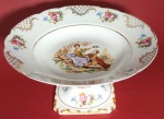 Fruteira em porcelana branca D&D com pé alto, filetes dourados imagens galantes medindo 23x13 cm.