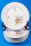 Seis pratos de sobremesa em porcelana branca com flores e filetes dourados e borda canelada medindo 17 cm.