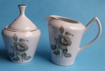 Açucareiro e cremeira em porcelana Pozzani com filetes dourados e flores e botões de rosa medindo 14x6 cm e 14x11 cm.
