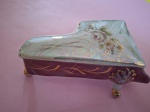 Antigo porta joias em porcelana com formato de  piano  nas cores branca furtacor e rosa com três pezinhos ,arabescos filetes dourados medindo 15x5 cm.