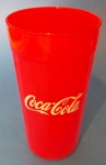 Copo em vidro na cor vermelha com símbolo da Coca-cola medindo 14x8 cm.