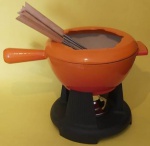 Panela de Fondue Gourmand Le Creuset na cor laranja em ferro fundido esmaltado com seis espetos em cabo de madeira com identificadores coloridos  medindo 31x10 e 26 cm os espetos.