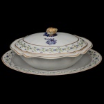 Companhia das Índias. Séc. XVIII - Legumeira com sua travessa de formato oblongo em porcelana chinesa. Fundo de superfície branca decorado em tons de azul por composição floral ao centro, e moldurado por guirlanda florida nos esmaltes verde e lilás. Pega da tampa em formato de fruto em policromia dourada. China. Dinastia Qing (1644 - 1911). Qianlong (1736-1795). 13 x 28 x 23 cm (legumeira). 34 x 26 cm (travessa)