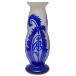 DEGUE - DAVID GUÉRON (1892-1950) - Vaso Art Déco em pasta de vidro acidado, de formato alongado com suave abaulado à meia altura, lavrado em cameo e ornamentado por folhagens e volutas estilizadas em azul Royal sobre fundo leitoso. Bojo encimado por borda revirada. Pé circular largo e liso. Assinado Degué na parte inferior do bojo e marca gravada Made in France sob a base. Criação da manufatura Verrerie dArt Degué, fundada em Paris pelo mestre vidreiro e artista espanhol David Guéron e ativa de 1926 a 1939. 43 x 13 cm.