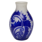 DEGUÉ - Vaso Art Déco em pasta de vidro acidado, lavrado em cameo e ornamentado por folhagens e volutas estilizadas em azul Royal sobre fundo leitoso. Bojo encimado por borda revirada. Assinado Degué na parte inferior do bojo e marca gravada Made in France sob a base. Criação da manufatura Verrerie d Art Degué, fundada em Paris pelo mestre vidreiro e artista espanhol David Guéron e ativa de 1926 a 1939. 21 cm.