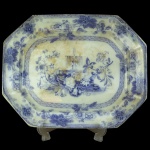 Travessa de porcelana inglesa apresentando apresenta decoração em azul e branco com bordas oitavadas e cantos chanfrados. Padrão floral e cenários centrais são características comuns do estilo. 43 x 34 cm. Apresenta desgastes na policromia e restauro.