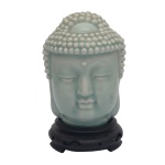 Escultura em porcelana possivelmente chinesa, revestida por coberta monocromática celadon, representando cabeça de Budha. Acompanha peanha em madeira. 17 x 13 x 12 cm.