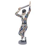 B & G DENMARK  Estatueta em porcelana dinamarquesa policromada, representando figura carnavalesca com vestes quadriculadas e espada na mão. Marca da manufatura de Copenhagen com numeração sob a base. 28 x 10 cm. A Royal Copenhagen foi fundada em 1775, em Copenhague, sob o patrocínio da rainha viúva Juliane Marie. A marca dinamarquesa foi estabelecida como a Fábrica Real de Porcelana para produzir porcelanas de alta qualidade, inicialmente focando na decoração em azul sob o vidrado e o padrão "Blue Fluted Plain". Seu símbolo distintivo, as três linhas onduladas que representam os três estreitos que cercam a Dinamarca, também remonta às origens da empresa.