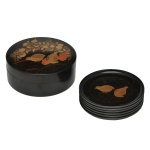 Caixa circular contendo 6 porta copos em madeira laqueada de preto. Apresenta um design decorativo na tampa retratando codornas (quail) em tons dourados e avermelhados. É acompanhado por um conjunto de pequenos porta-copos (coasters) também lacados com motivos semelhantes. 4 x 12 cm caixa / 10 cm porta copos.