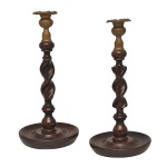 Par de originais castiçais com hastes retas e espiraladas, apoiadas em anelados. Arrematadas superiores em bronze polido, no formato de vasos com bobeches bordadas por largas abas. Bases circulares com centros côncavos. 30 x 14 cm.