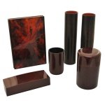 Conjunto de peças para banheiro em laca je outros materiais com acabamento em tons de marrom-escuro e detalhes avermelhados translúcidos. Esta técnica tradicional de lacagem cria uma superfície altamente polida e durável. O conjunto é composto por 4 vasos cilíndricos (altos e baixos), Caixa organizadora retangular com tampa e 1 Espelho articulado com três painéis (24 x 16 cm (fechado) / 24 x 48 cm (aberto). 25 cm / 15 x 9 cm / 10 x 7 cm / 4 x 17 x 7 cm