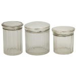 Conjunto de 3 potes cilíndricos para toucador, de tamanhos diversos, em cristal moldado com gomos e filetes. Apresentam tampas em prata lavrada. Contrastes, sendo 2 ingleses  e um francês Cabeça de Minerva.