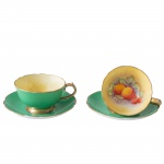 Par de xícaras com seus pires em porcelana inglesa. Apresenta uma esmaltagem de tom verde na parte externa com detalhes em ouro. Interior decorado com um padrão de frutas.