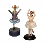 COWPARADE  Lote constando 2 figuras colecionáveis em miniatura da exposição CowParade, sendo:A) Figura em resina de caixinha de música giratória, intitulada "Bovina at the Ice Cowpades". Fabricada pela Westland Giftware e apresenta uma vaca vestida de patinadora artística sobre uma base. A peça é feita de resina e toca a melodia "Music Box Dancer". Este modelo específico foi aposentado pela fabricante em julho de 2007. 23 x 13 cm.B) Figura de vaca bailarina "Moo Moo in a Tutu", lançada em 2003 e atualmente aposentada. 21 x 10 cm.