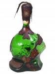 VIDRO ITALIANO, uma (1) garrafa decorativa em vidro verde, de formato bojudo, com aplicações em couro trabalhado e tachas metálicas, apresentando alça superior e ornamentos em estilo rústico, apresenta desgastes, vendida  no estado da foto, medindo 29cm.