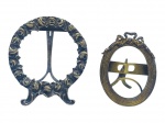 BRONZES, dois (2) pequenos porta retratos confeccionados em bronze, sendo: A) 1 redondo, cinzelado por flores e folhagens, ausência do vidro e da tampa traseira, medindo 7,5x6,5cm e B) 1 oval cinzelado em caneluras encimado por laçarote em vazado, ausência do vidro e da tampa traseira, medindo 6,5x4,5cm.
