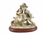 ESCULTURA, um (1) grupo escultórico confeccionado em resina italiana representando cena infantil com duas crianças e carrinho de mão com pintura em policromia, apoiada sobre base oval em madeira, medindo 24x27x14cm.