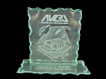 VIDRO, um (1) troféu confeccionada em vidro transluicido lapidado, com base retangular e placa vertical de bordas onduladas, apresentando gravação da AVLRJ  Associação de Voo Livre do Rio de Janeiro, com desenho do Pão de Açúcar e referência ao Brasil/Rio. Base com inscrição de homenagem ao secretário de urbanismo Alfredo Sirkis, medindo 20x23x9cm, 1 bicado na base.