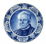 FAIANÇA DELFT, um (1) prato confeccionada em faiança vitrificada de origem holandesa, estilo Delft Blue, com decoração em azul e branco, apresentando ao centro retrato de Johannes Paul II / Karol Wojtyla, Papa João Paulo II. Borda ricamente ornamentada com motivos florais e arabescos. Verso com marcação Origineel Delftsblauw Handwerk, Delft, made in Holland, medindo 24cm.