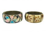 BIJUTERIAS, dois (2) braceletes confeccionados em placas de osso de modelos distintos, sendo 1 com decoração geométrica em policromia com armação em metal dourado, apresentando falhas, vide foto, medindo 7,5cm e 1 com pintura floral na tonalidade marrom, apresenta leves falhas no osso, monture em metal dourado, medindo 7,5cm.