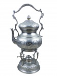 METAL PRATEADO, um (1) samovar confeccionado em metal espessurado a prata com rico cinzelado de flores e folhagens, corpo bojudo, alça central fixa, apoiada sobre base com hastes em arabescos, acompanha fogareiro, apresenta falhas no banho, medindo 46,5x24cm, apresenta 2 leves mossas no bojo.