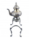 METAL PRATEADO, um (1) samovar confeccionado em metal espessurado a prata com rico cinzelado por elementos vegetalistas, pega da tampa no feitio de pinha, base tripoide finalizados em garra com ausência do fogareiro, apresenta falhas na prateação e alça central solta, necessitando solda, medindo 37x23cm.