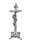 METAL PRATEADO, um (1) paliteiro representnado fidalgo confeccionado em metal espessurado a prata, base quadrangular com pés em garra, prato superior em vazados, encimado por pinha, medindo 22cm de altura.