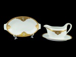 Tirschenreuth (Baviera, Alemanha), duas (2) peças confeccionadas em porcelana alemã na tonalidade branca, decorada por faixa perolada e elementos vegetalista em vasta douração com pintura de flores e folhagens em policromia, sendo: A) 1 covilhete, medindo 25x14,5cm, fio de cabelo na borda e B) 1 molheira fixada ao presentoir, medindo 11,5x21x15cm.