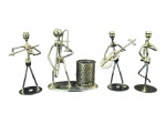 ESCULTURAS, quatro (4) figuras de músicos estilizados confeccionados em metal fosco, cada uma com instrumento musical, sendo uma delas integrada a base com porta-canetas/porta-objetos cilíndrico vazado, medindo 14/13cm. Falhas na prateação e sinais de oxidação.