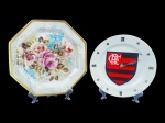 PORCELANAS, lote com dois (2) pratos decorativos confeccionados em porcelana na tonalidade branca, sendo: A) 1 oitavado com pintura de flores e folhagens em policromia e borda filetada a ouro, medindo 31cm de diâmetro e B) 1 com pintura do Flamengo, adaptado para relógio de parede, peças em plástico prateado em algarismos romanos com quebra no ponteiro, não testado e sem garantia de funcionamento, medindo 25,5cm.