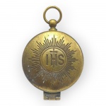 ARTE SACRA, uma (1) teca eucarística porta-hóstia, da marca Eberle, confeccionada em metal dourado, de formato circular, com argola superior e tampa articulada. Frente decorada em relevo com raios e monograma cristológico IHS. Objeto litúrgico utilizado para acondicionar e transportar hóstias consagradas, sinais de uso e leves oxidações, risco interno, vide foto, medindo 4,5cm de diâmetro.