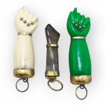 BIJUTERIAS, lote com três (3) pingentes representando figas tradicionais confeccionados em material sintético nas cores marfim e verde, uma em ágata na tonalidade marrom, com aplicações e acabamentos em metal dourado, sinais de uso, maiores medindo 3,5cm e menor 3cm.