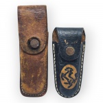 DIVERSOS, dois (2) estojos para canivete confeccionados em couro, sendo um na tonalidade marrom, fecho em metal com sinais de oxidação e falhas no couro, medindo 14,5x5cm e uma em couro na tonalidade preta com decoração representando cavalo, fecho metálico com sinais de oxidação, medindo 11,5x5cm.