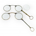 COLECIONISMO, dois (2) pince-nez, tipo lorgnette, com lentes circulares, armações em metal dourado e cabos alongados ornamentados, terminados em aros para apoio, um necessita solda no aro e 1 lente solta, medindo 12x10x4cm e 1 em excelente estado, marcado SANTOS no corpo, medindo 13x11x4cm.