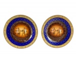 FSK (Friedrich Simon) Tchecoslováquia, par (2) de pratos decorativos confeccionados em porcelana theca na tonalidade branca, decoradas por espessas faixas na tonalidade azul cobalto e creme, decorada por guirlanda floral e geométrica em policromia e ouro, centro reservando cena mitológica em policromia, apresentam leves falhas na pintura e douração, medindo 16,5cm.