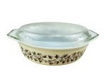 PYREX AMERICANO, um (1) pyrex oval com tampa confeccionado em vidro opalinado na tonalidade branca com pintura na tonalidade creme, decorado por guirlanda vegetalista em ouro, medindo 11x33x22cm.