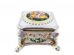 CAPODIMONTE, uma (1) caixa porta joias confeccionada em faiança italiana, assinado por R.S. MARINO, moldado em perolados, cena ninfa com carrancas e elementos florais em policromia e relevo, sinais de craquele, fio de cabelo na tampa e interior com brasão filetado em ouro, medindo 8x11,5x11,5cm.