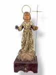ARTE SACRA, um (1) imaginário confeccionado em madeira entalhada a mão representando Menino Jesus de Praga, patina envelhecida com realces em dourado, apoiada sobre base com pintura vermelha e recortes nos pés, resplendor e cruz em metal dourado, medindo 27,5cm de altura.