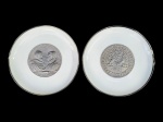 Hutschenreuther, dois (2) pratos decorativos confeccionados em porcelana alemã na tonalidade branca, feitos para Munich Re (é uma das maiores companhias de resseguro do mundo em termos de prêmio subscrito), sendo 1 decorado por Duque Guilherme V da Baviera e sua esposa, Renée de Lorena e outro "Munchener Ruck" do Duque Albert V, ambos com pintura prateada e filetes na borda, medindo 14,5cm de diâmetro.
