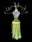 DIVERSOS, um (1) suporte para bijuterias confeccionado em acrílico translucido e verde representando nu feminino com saia em pendantes de tecido sintético e missangas, apresenta bicado na vase e folga na parte superior, vide foto, medindo 30cm de altura.