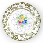 PORCELANA, um (1) prato decorativo confeccionado em porcelana na tonalidade branca com pintura de flores e folhagens em policromia, borda em elementos florais e vegetalistas em vasta douração com pequenas falhas, medindo 23cm de diâmetro.