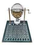 DIVERSOS, um (1) bingo, composto por base em madeira pintada na cor verde com tabela numérica de 1 a 75, globo giratório em metal aramado com sinais de oxidação, manivela lateral e bolinhas em madeira numeradas em seu interior, sinais de uso e leves falhas, medindo 27x45x30cm.