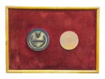 QUADRO/MEDALHAS, um (1) quadro em moldura dourada, fundo em tecido aveludado vermelho, contendo duas medalhas comemorativas em bronze, sendo uma com inscrição Participante e outra com representação de edifício em relevo, apresentando sinais de oxidação, manchas no tecido, marcas e desgastes compatíveis com o uso e o tempo, medindo 17,5x24,5cm.